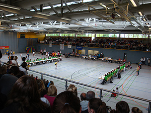 Bei den DM im Rope-Skipping Freestyle in Frankenthal, Springerin srpingt in einem Feld in der Turnhalle über ein Seil, links und rechts eine Reihe mit 4 Tischen an denen je ca. 14 Kampfrichter sitzen, im Vordergrund sieht man die Zuschauer auf der Tribüne, von der das Bild gemacht ist, im Hintergrund sieht man die andere tribüne, die ebenfalls mit Zuschauern voll besetzt ist, jeweils hinter den Kampfrichtern springen sich die nächsten Teilnehmer warm