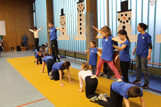 Mehrere Kinder bilden zusammen drei kleine Pyramiden auf einem Bodenläufer und präsentieren sich den Zuschauern.